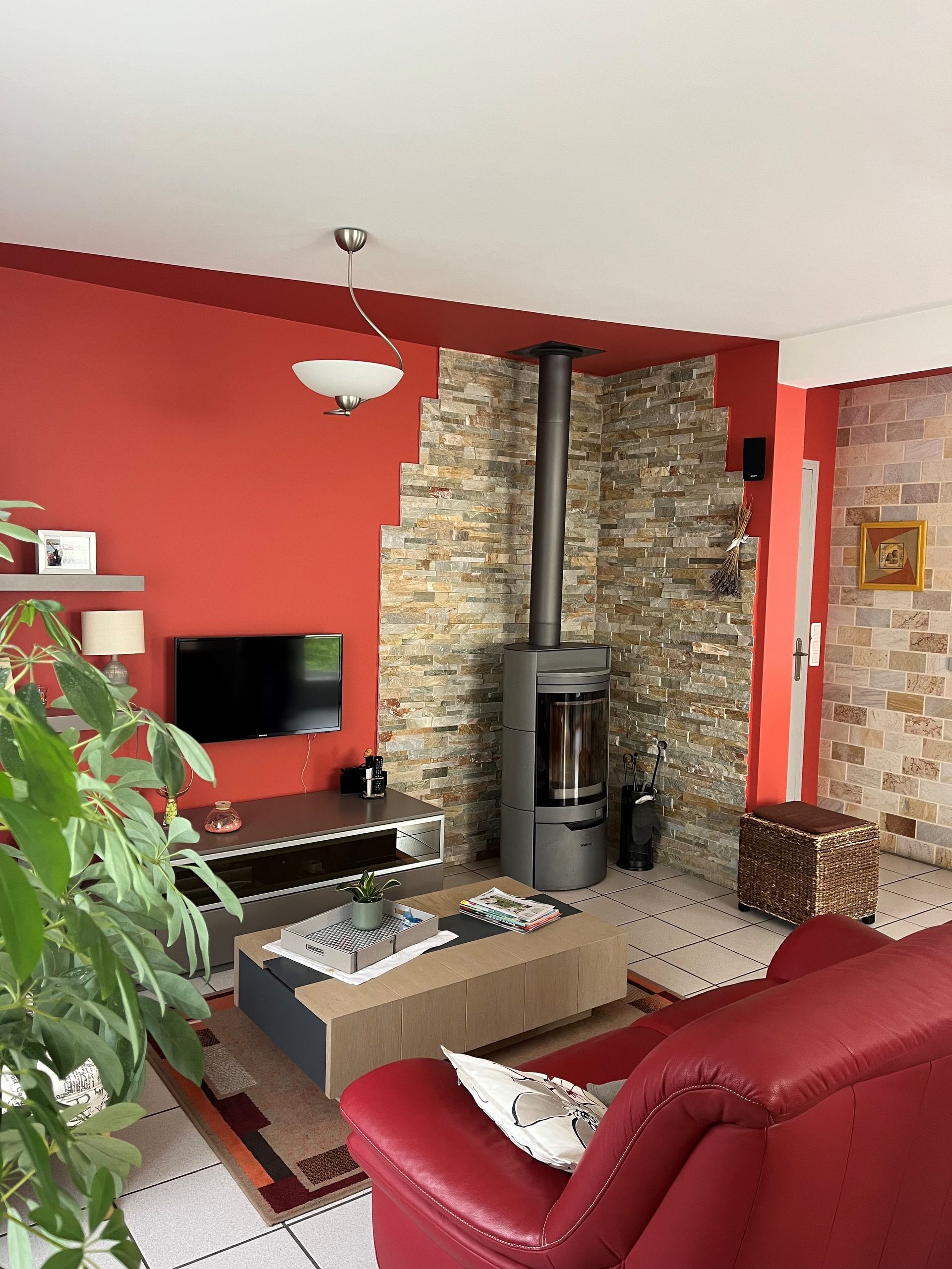 Salon chaleureux avec murs rouges, cheminée en pierre, télévision et canapé rouge.