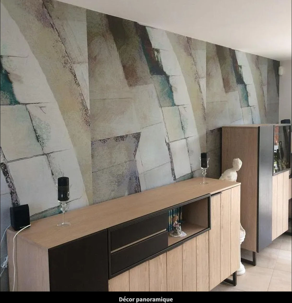 Salon moderne avec papier peint géométrique, console en bois, haut-parleurs et meuble près d'un buste de mannequin.