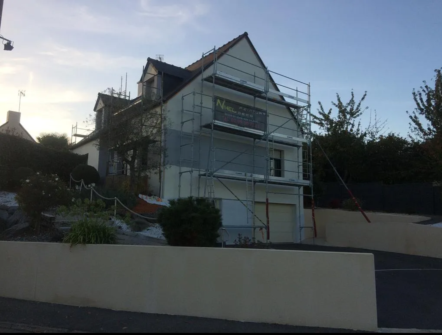 Maison en rénovation avec des échafaudages, vue de la rue au crépuscule.