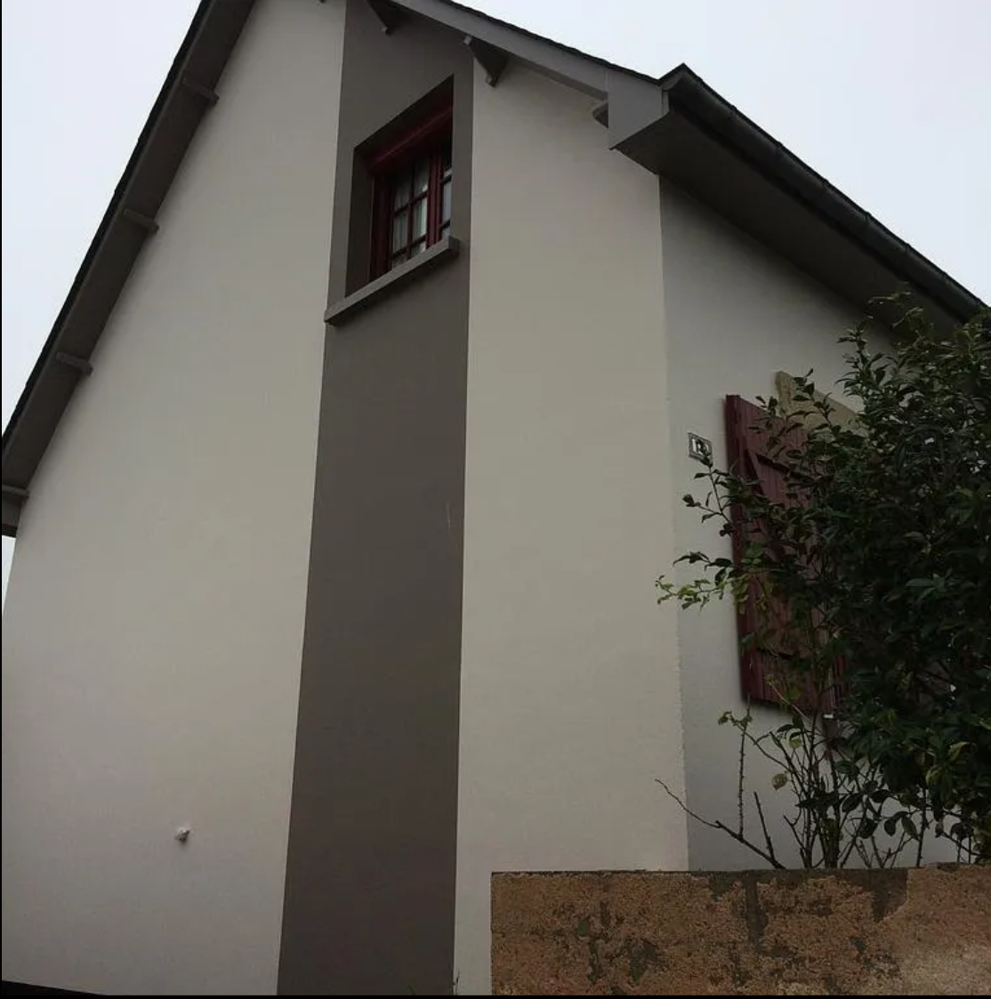 Extérieur de maison blanche avec une bande verticale grise, toit foncé et petite fenêtre près de la ligne de toit