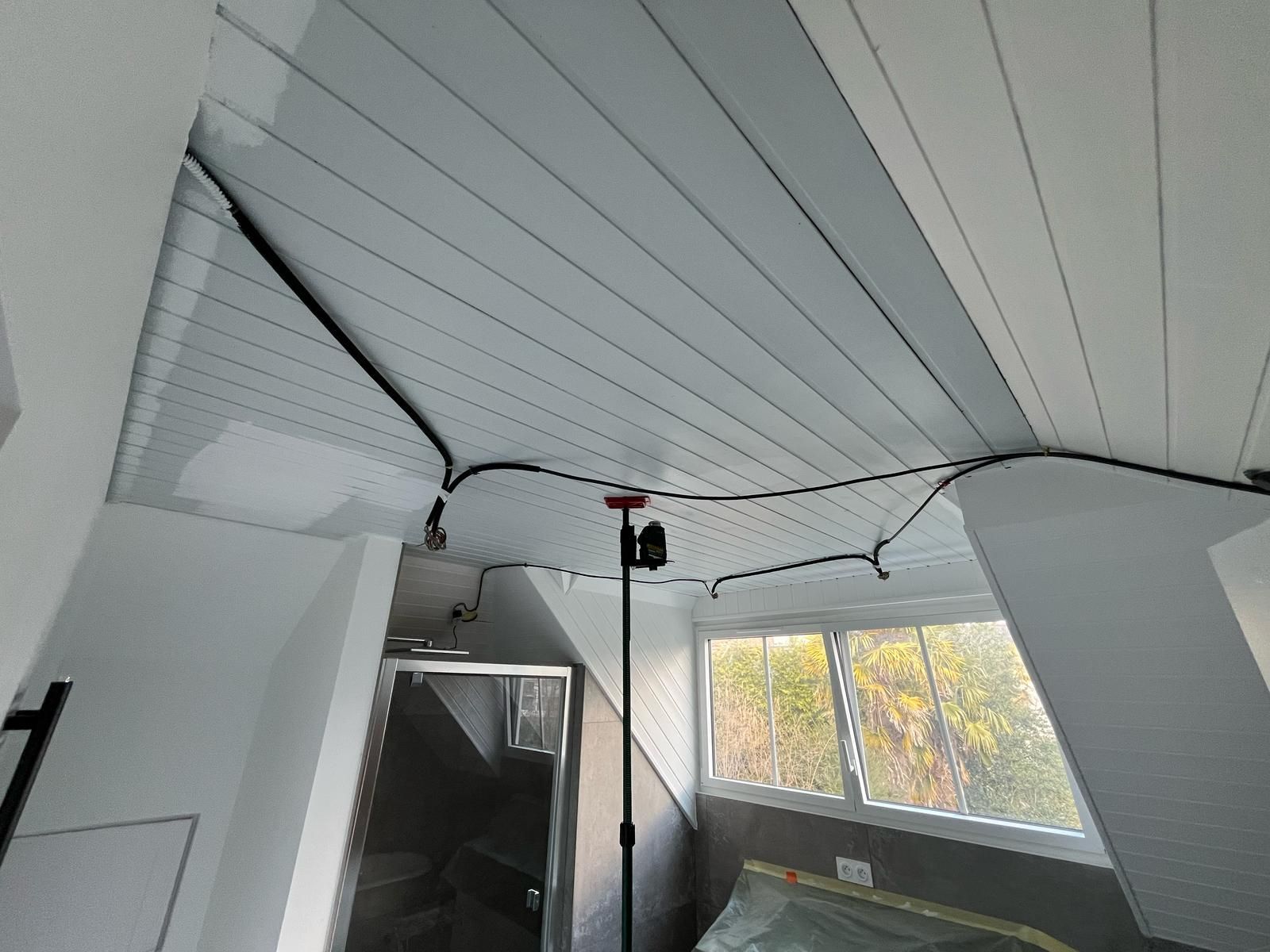 Plafond blanc abîmé avec des panneaux affaissés et des fils électriques apparents dans une pièce avec fenêtres