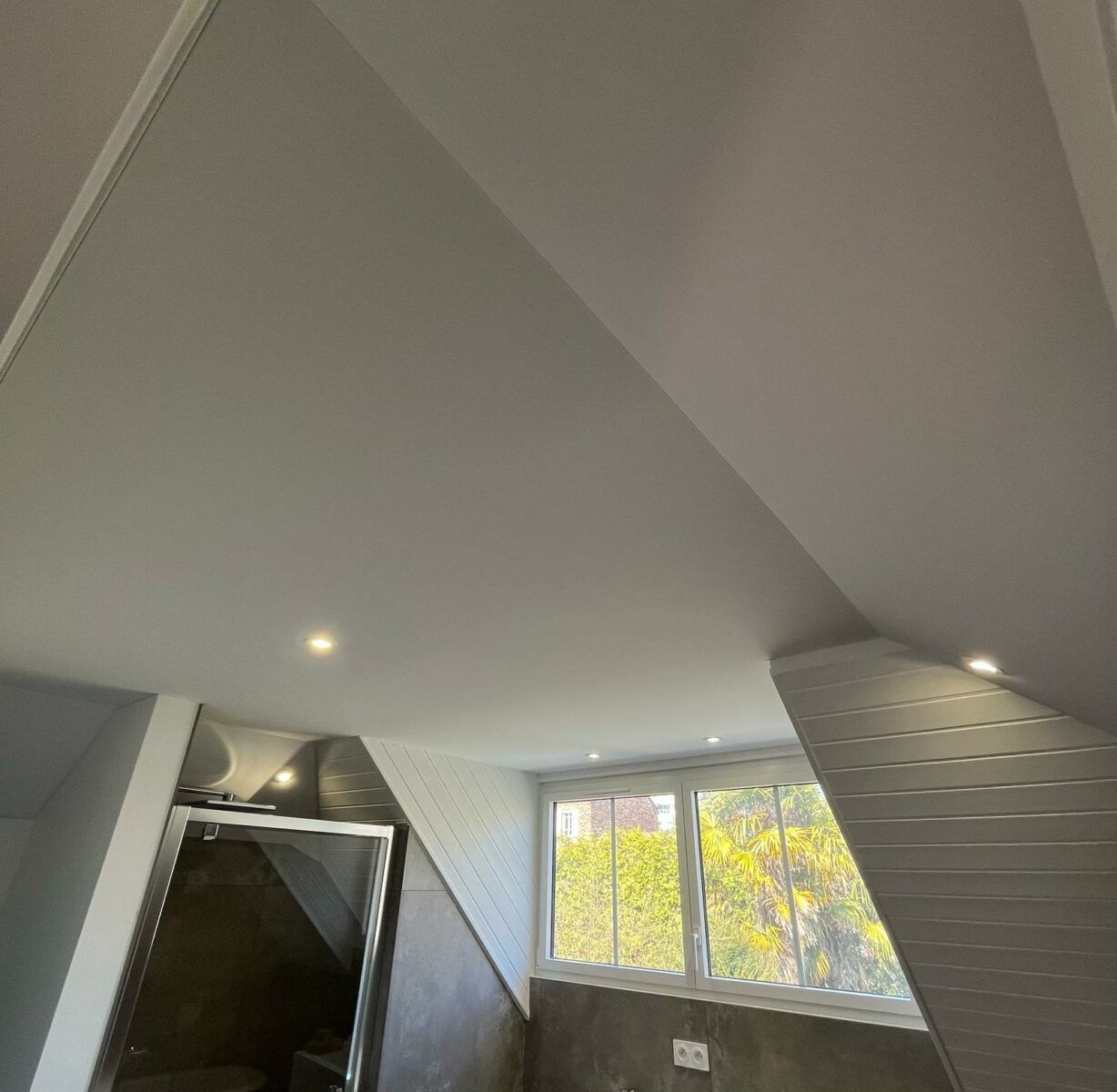Chambre mansardée avec plafond blanc en pente, spots encastrés, fenêtre et dressing ouvert