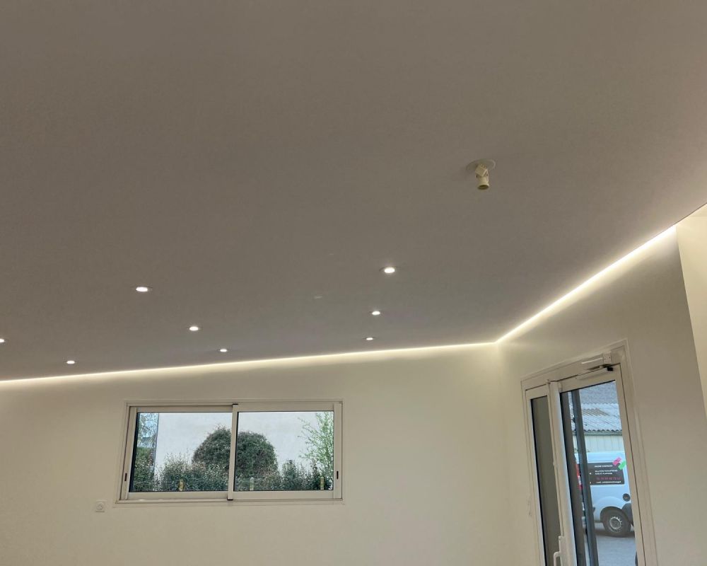 Pièce moderne et lumineuse avec spots encastrés au plafond, une fenêtre et une porte vitrée donnant sur l'extérieur.