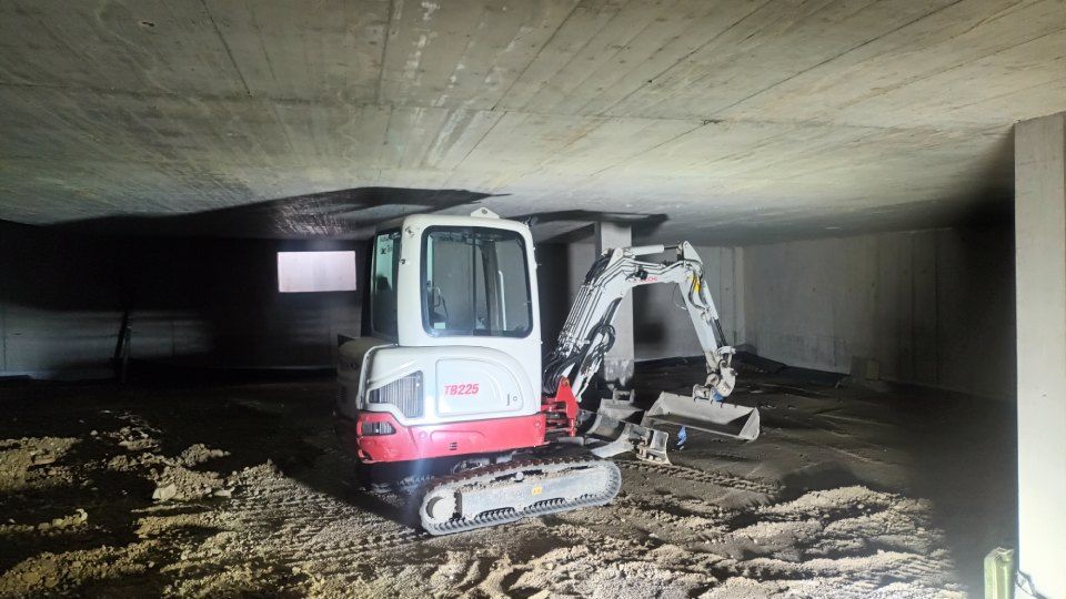 Kleinbagger gräbt in einem Betonbauwerk.