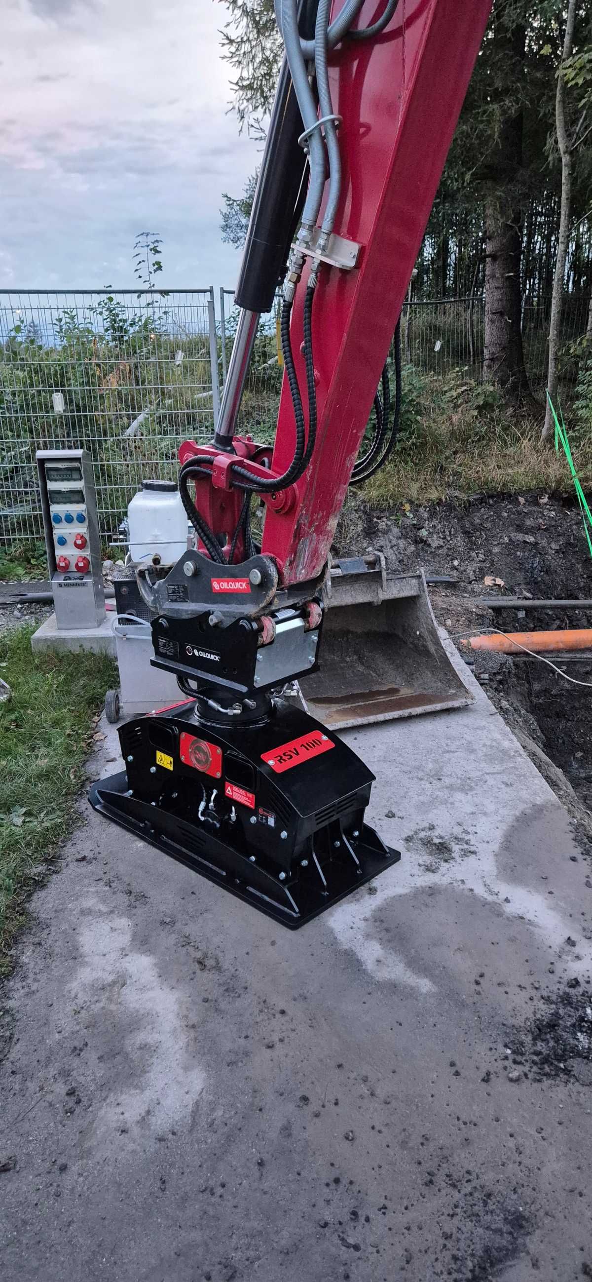 Ein Bagger verdichtet Asphalt auf einem Gehweg. Rote und schwarze Baumaschinen. Baustelle im Freien.