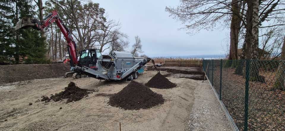 Ein Bagger sortiert Erde in der Nähe eines Zauns. Erdhaufen an einem sandigen, bewölkten Tag.