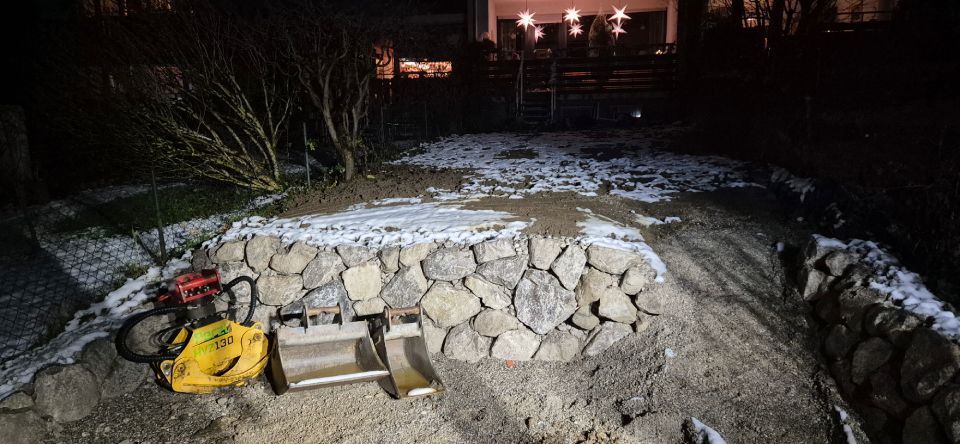 Nachts wird eine Steinstützmauer errichtet, im Hintergrund ist eine gelbe Verdichtungsmaschine zu sehen.