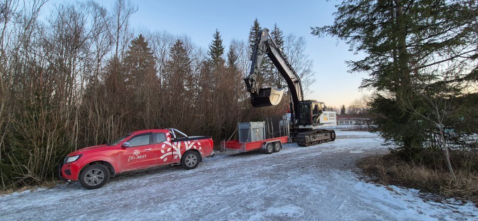 Roter Pickup-Truck mit Anhänger und Bagger in einem verschneiten Waldgebiet.