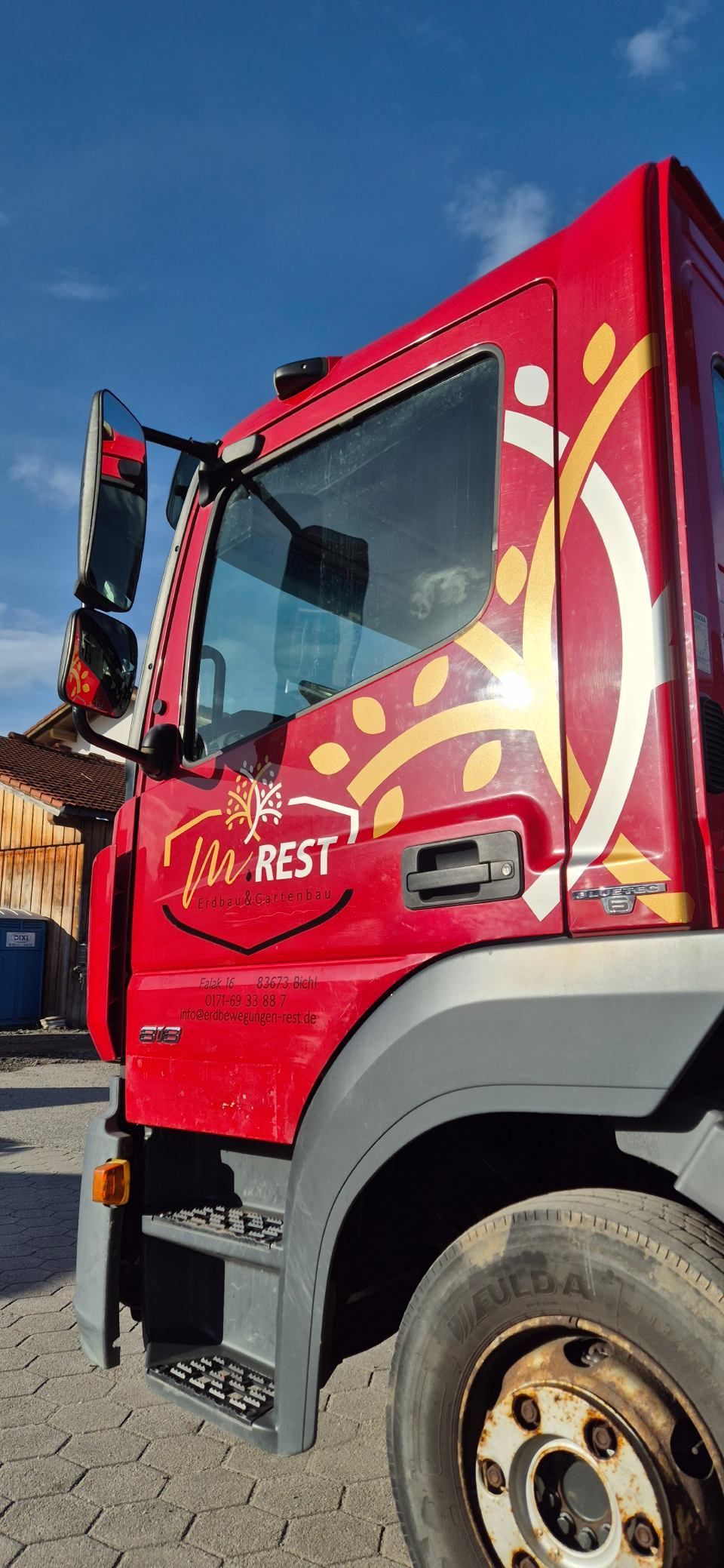 Roter Lastwagen mit Logo vor blauem Himmel.