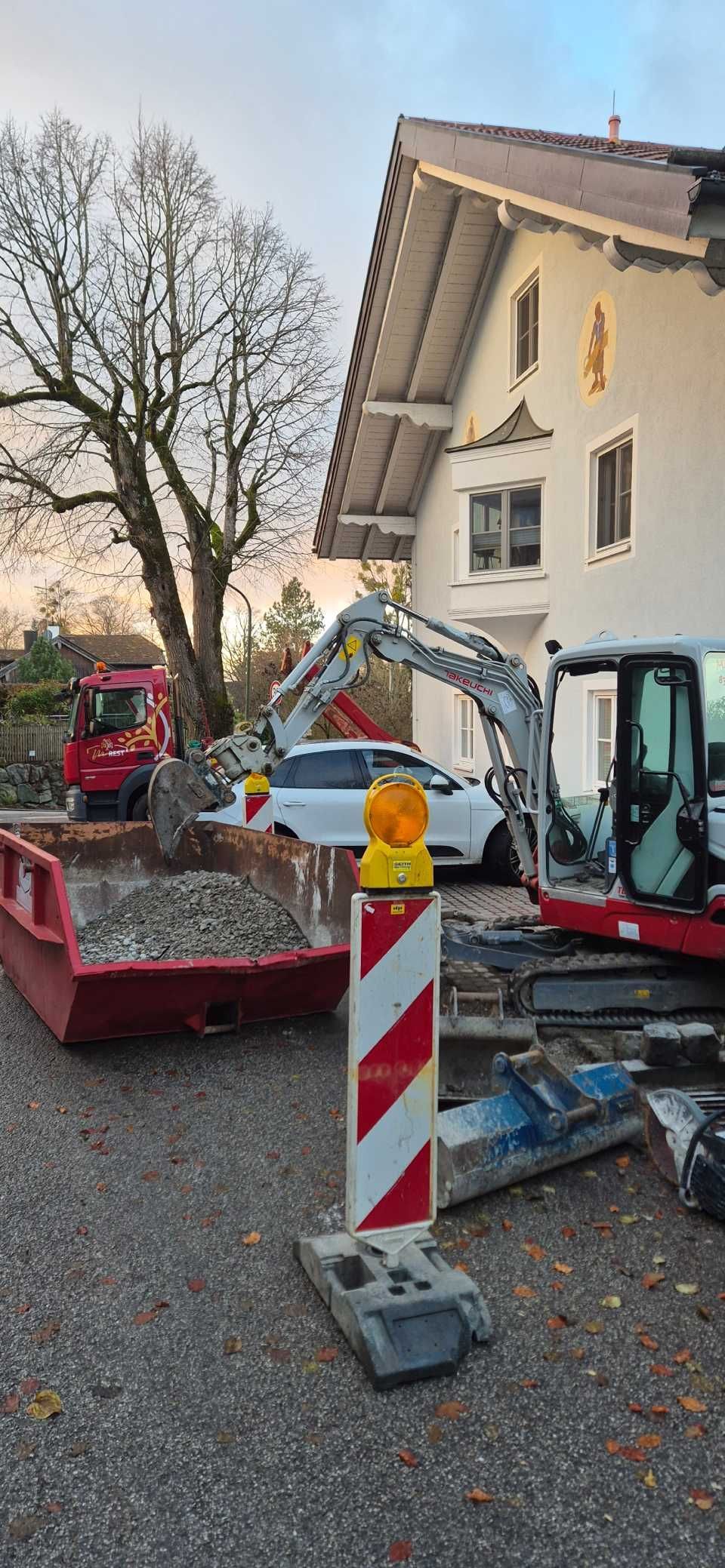 Baustelle mit Baumaschinen und einem weißen Auto vor einem weißen Gebäude. Ein Warnpfosten ist zu sehen.