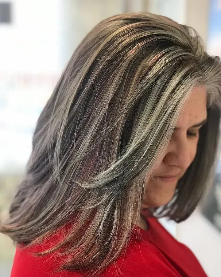 Una mujer con cabello gris y reflejos lleva una camisa roja.