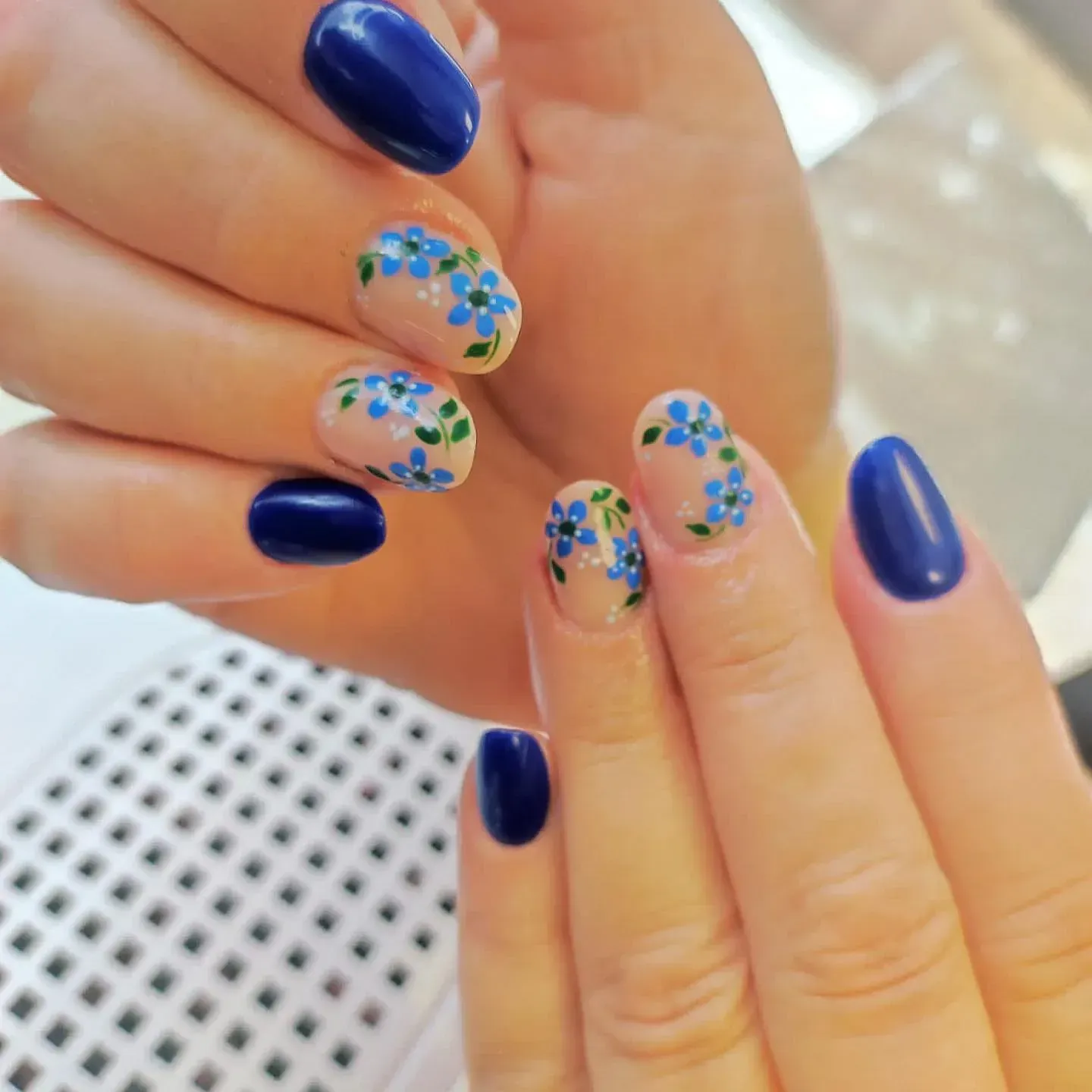 Un primer plano de las uñas de una mujer con flores azules en ellas.