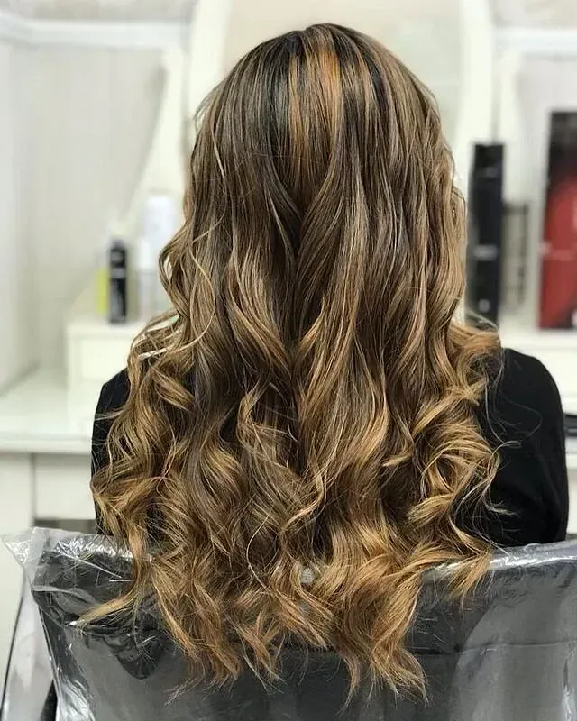 Una mujer con cabello largo y rizado está sentada en una silla en un salón.