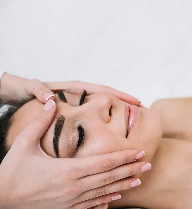 Una mujer está recibiendo un masaje facial con los ojos cerrados.