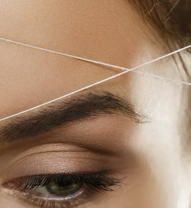 Un primer plano de las cejas de una mujer siendo enhebradas con hilo.