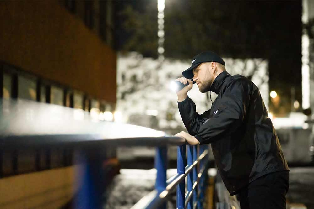 Sicherheitsdienst - Ein Mann in einer schwarzen Jacke und Hut hält eine Taschenlampe in der Hand .