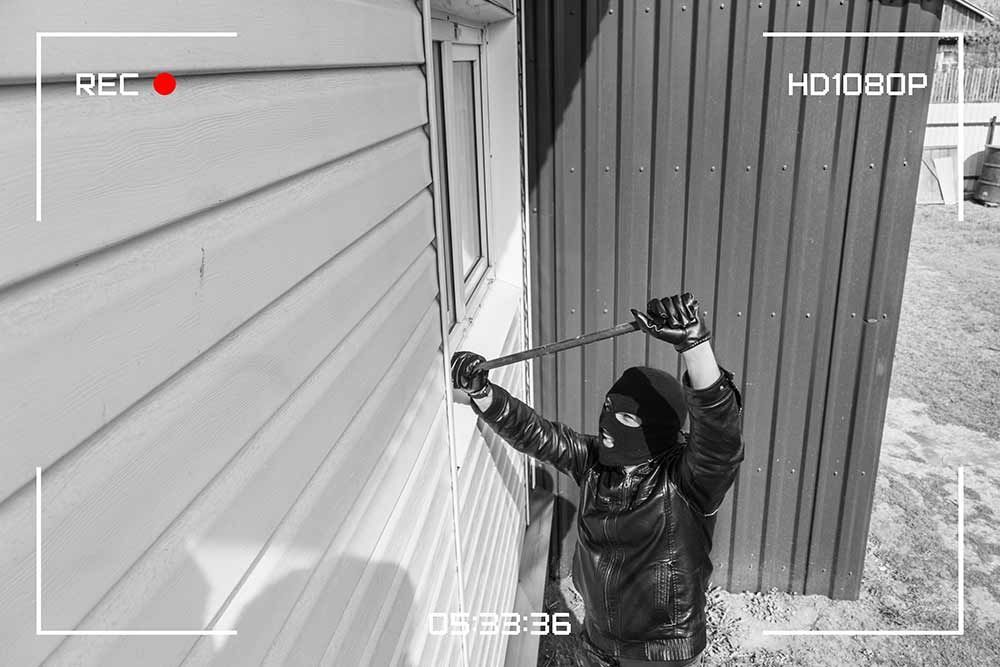 Alarmsysteme für Wohnhäuser - ein Foto eines Einbrechers , der ein Fenster mit einem Hammer öffnet