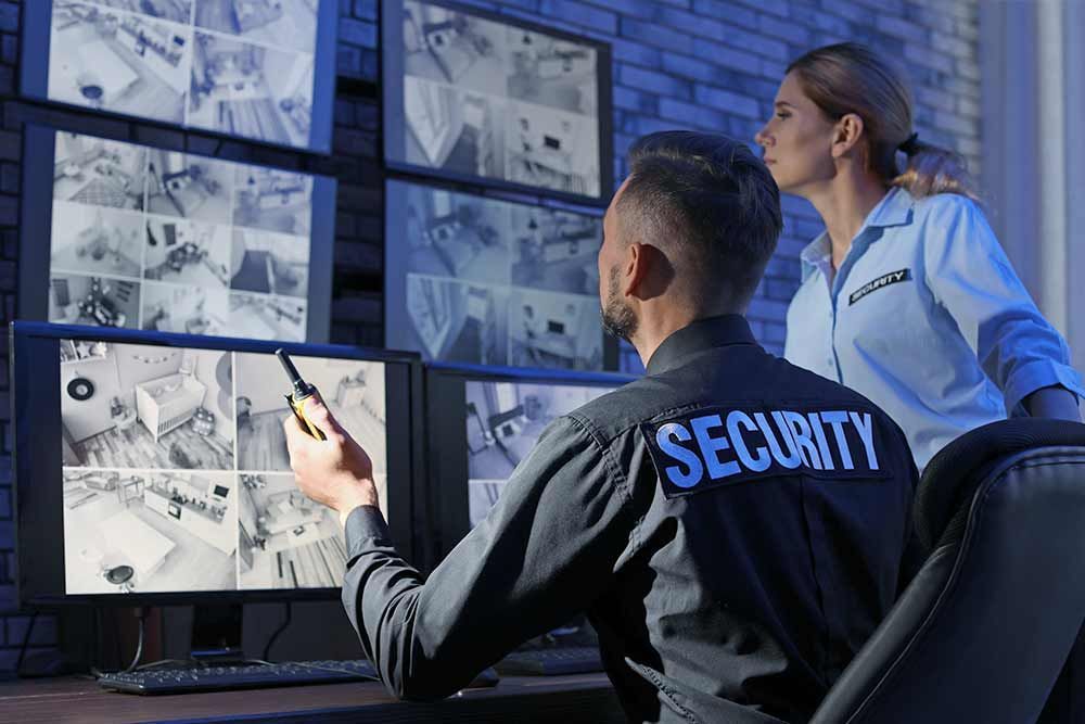 Moderne Videoüberwachungstechnologie - ein Mann und eine Frau in Sicherheitsuniform schauen auf Monitore