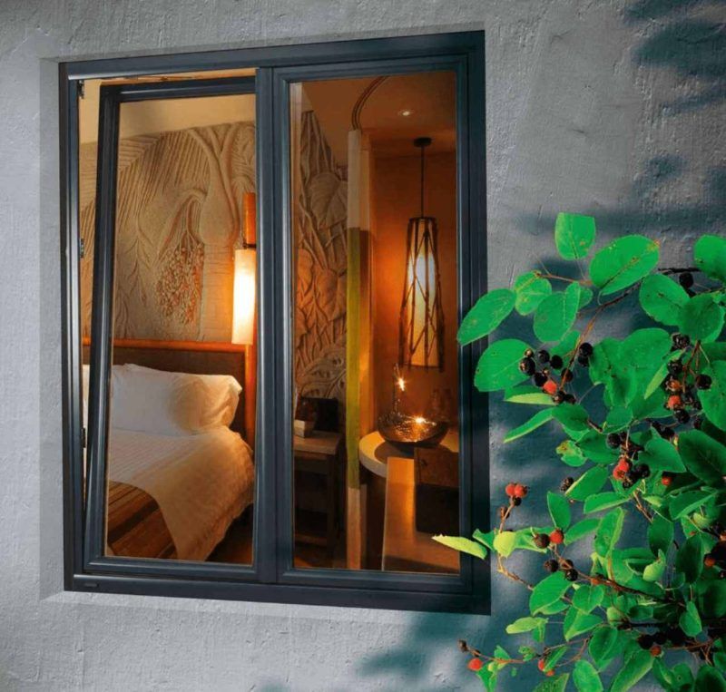 Une fenêtre à cadre sombre s'ouvrit en position inclinée, laissant entrevoir une chambre d'hôtel chaleureuse et faiblement éclairée, avec un lit et une lampe à l'intérieur.