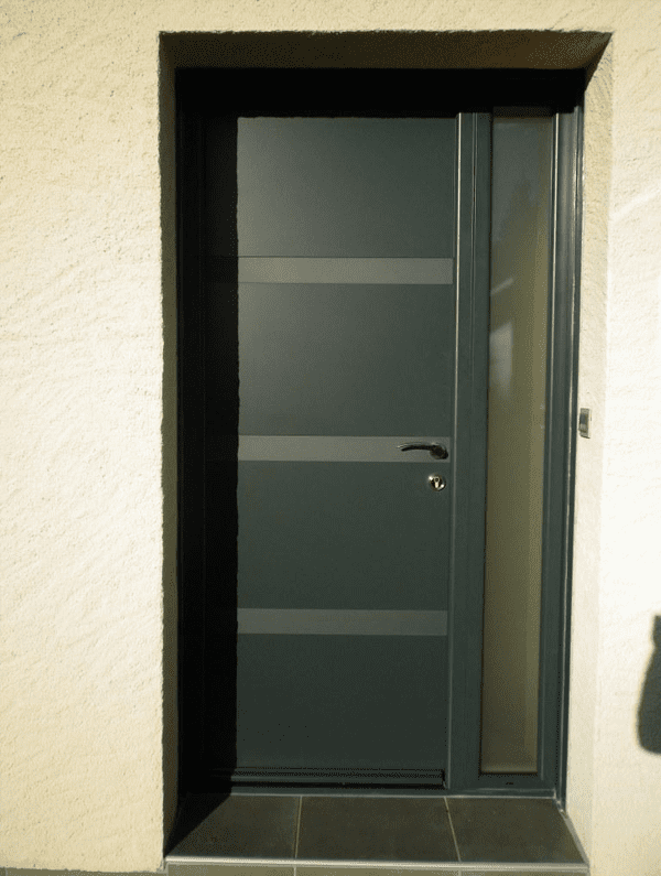 Une porte moderne gris foncé à panneaux horizontaux et une étroite imposte vitrée verticale latérale, intégrée à un mur en stuc clair.