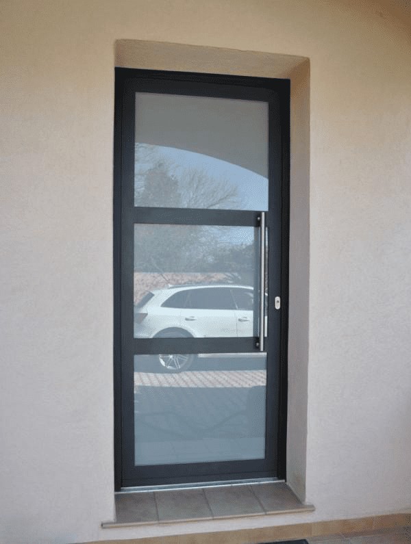 Une porte vitrée moderne à cadre noir, composée de trois panneaux horizontaux et d'une longue poignée verticale argentée, encastrée dans un mur beige.