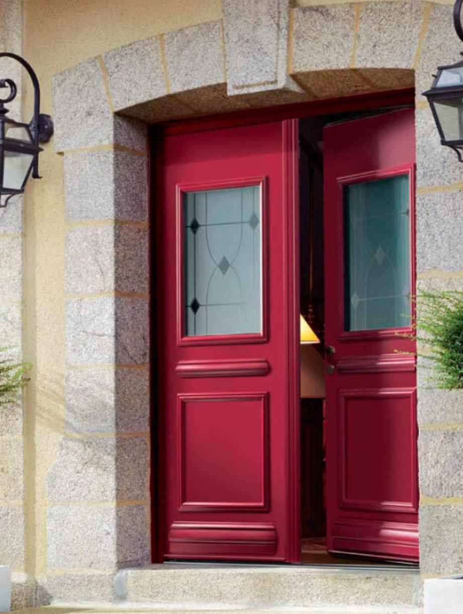 Deux portes doubles à panneaux rouges avec inserts en verre, encadrées d'une structure cintrée en pierre, partiellement ouvertes.