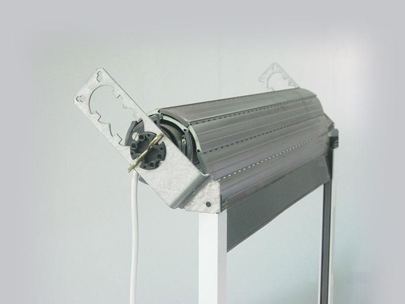 Un mécanisme de volet roulant métallique avec des supports de boîtier blancs, monté sur le dessus d'un cadre de fenêtre.