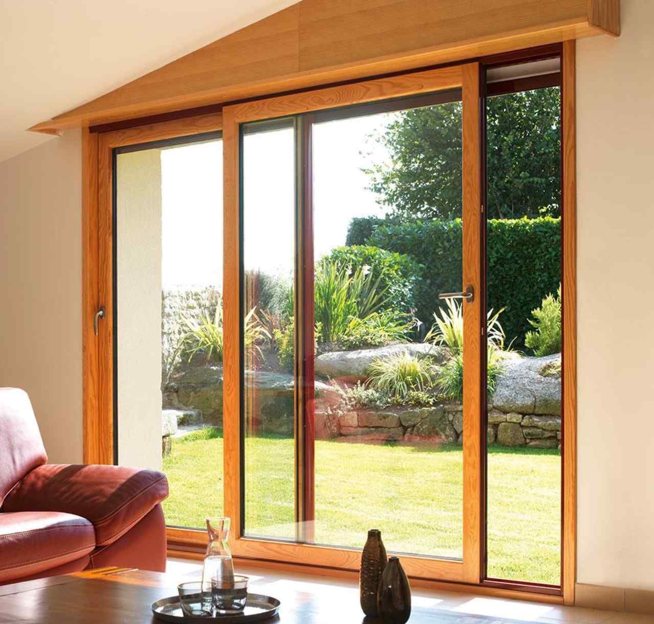 Des portes-fenêtres coulissantes en bois s'ouvrent sur un jardin ensoleillé, avec un canapé rouge au premier plan.