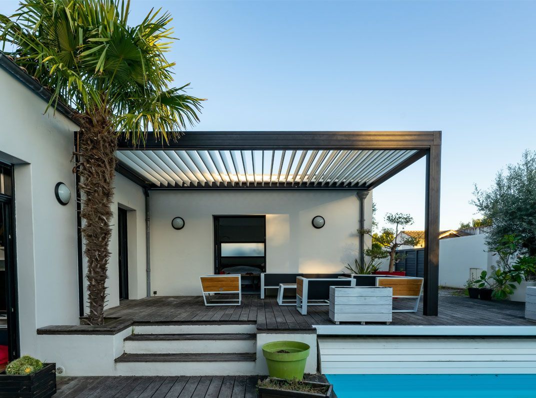 Une terrasse moderne avec une pergola à persiennes, des sièges d'extérieur et une petite piscine sous un ciel d'un bleu éclatant.