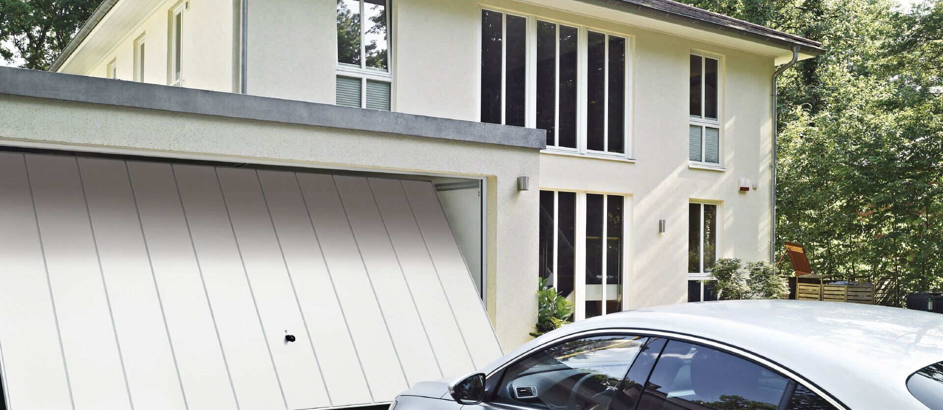 Une maison blanche avec une porte de garage blanche moderne, partiellement ouverte, et une voiture blanche garée dans l'allée.