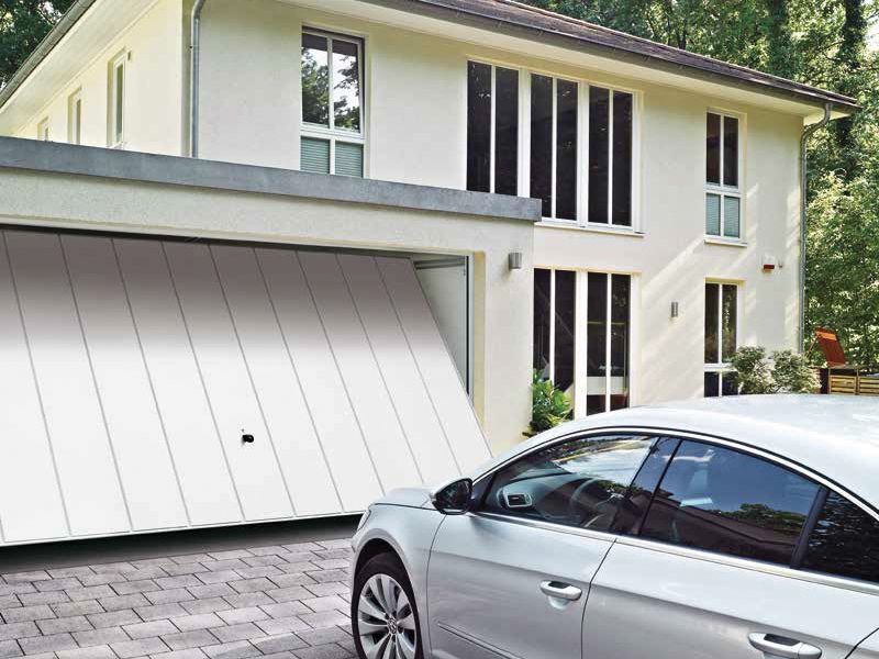 Une voiture argentée garée devant une maison moderne avec une porte de garage blanche ouverte.