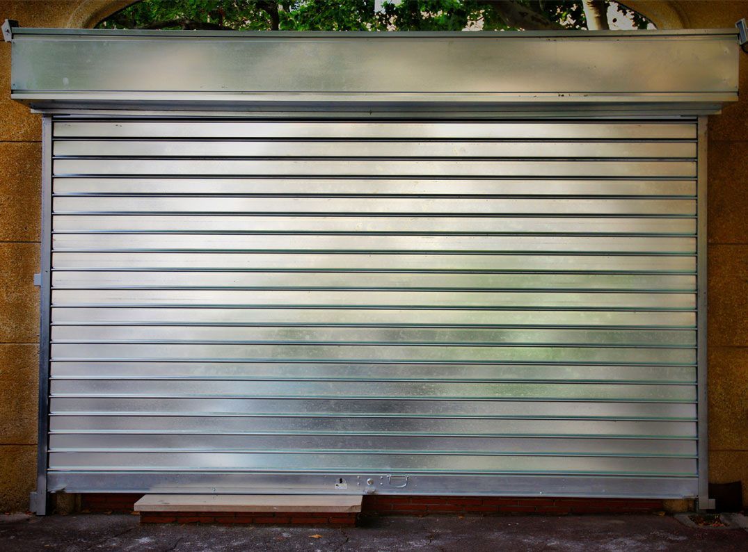 Une porte de sécurité métallique à enroulement fermée, installée à l'entrée d'un bâtiment.