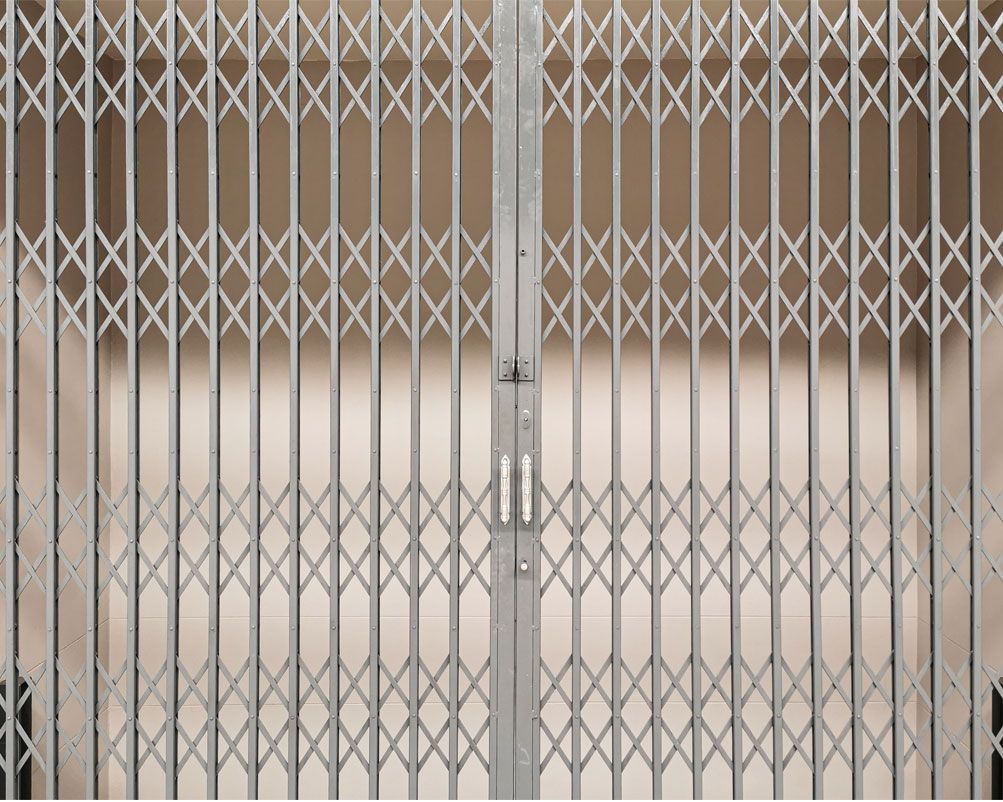 Un portail de sécurité rétractable en métal gris, orné d'une structure en treillis à motif losange, se referme sur un fond uni.