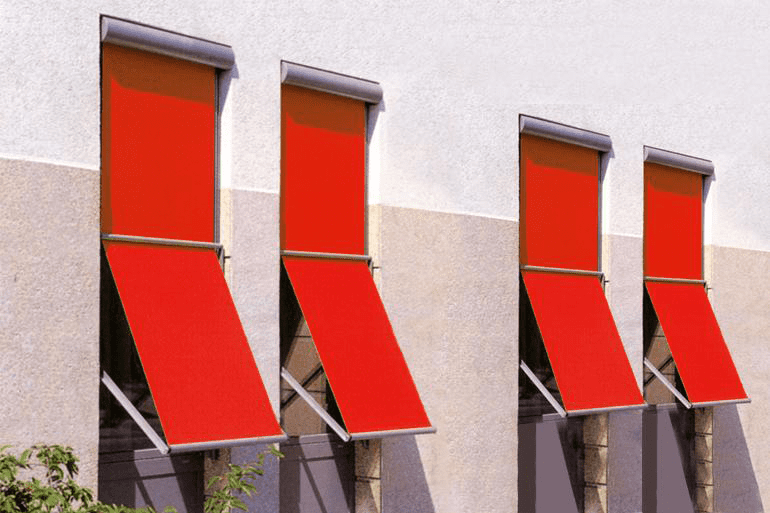 Quatre auvents de fenêtre extérieurs rouge vif étaient déployés en angle sur le mur clair d'un bâtiment.