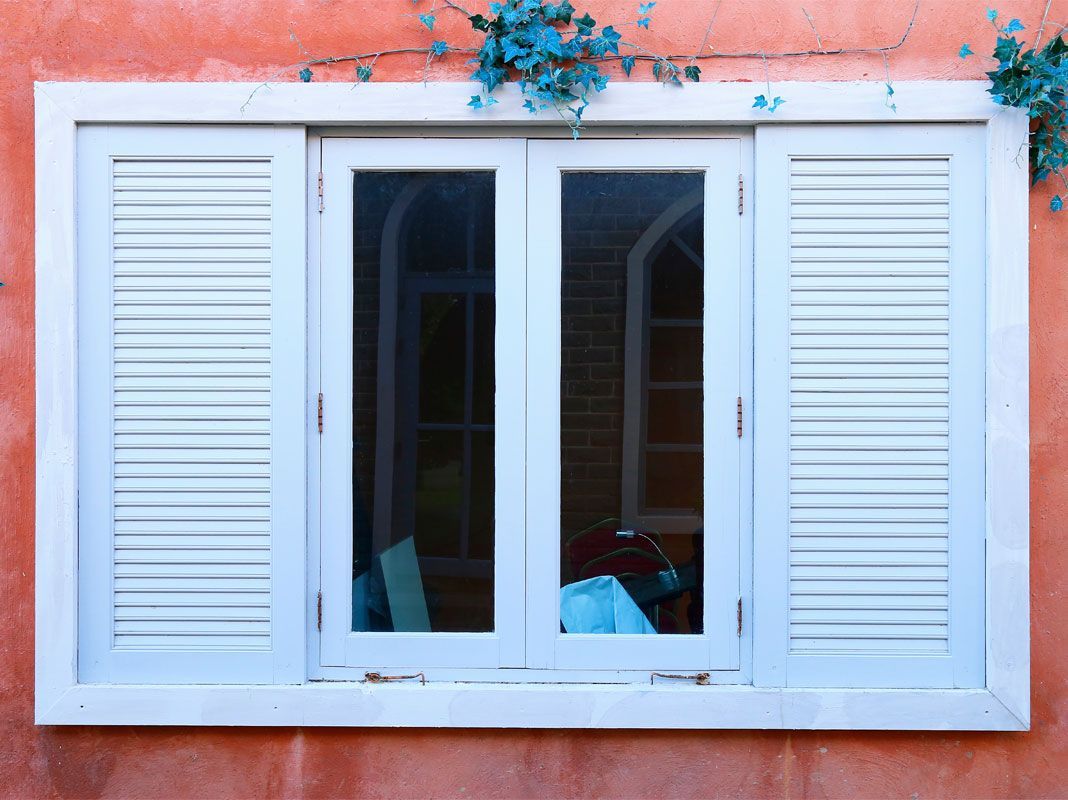 Fenêtre blanche à persiennes sur un mur texturé de couleur orange.