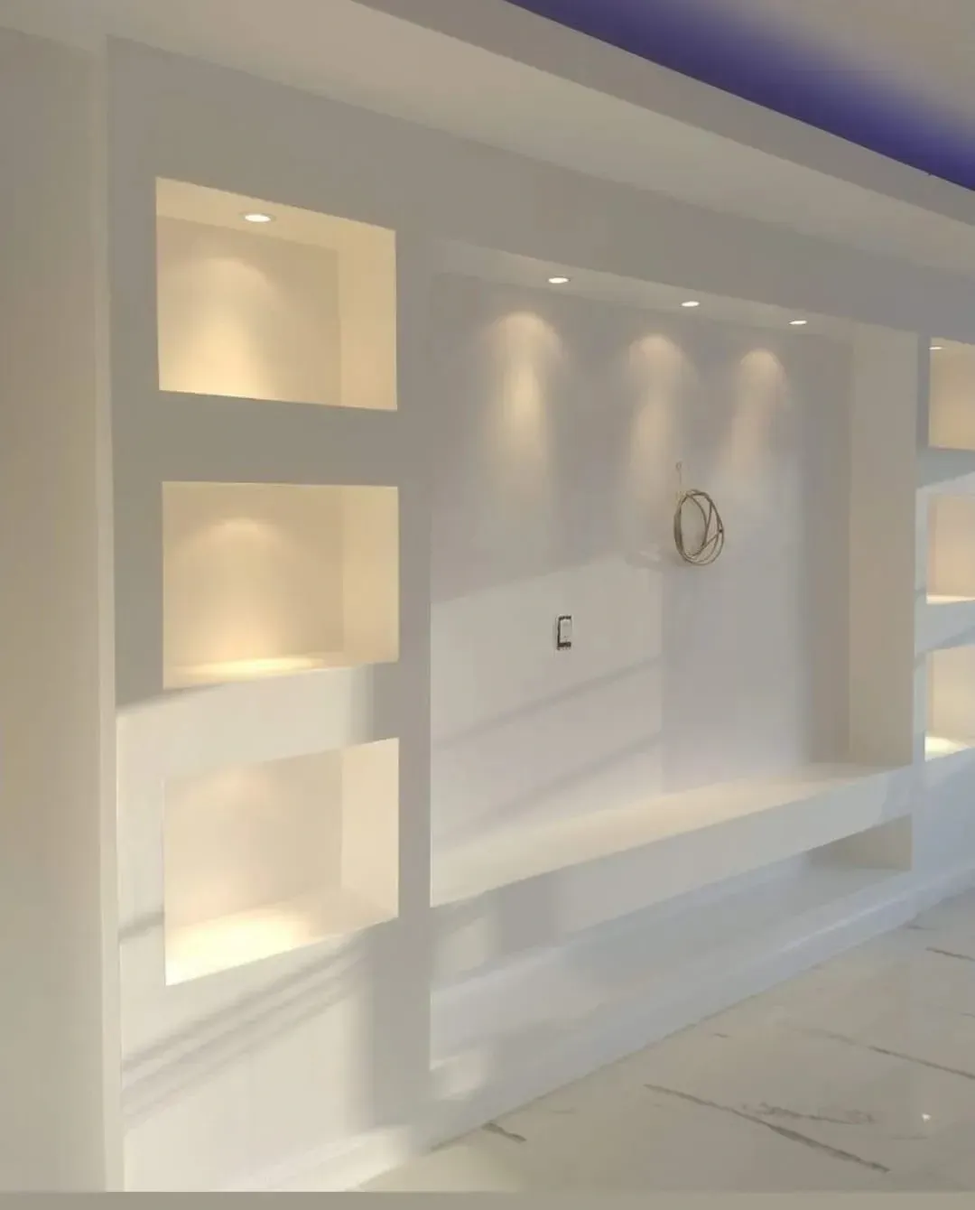 Una pared interior blanca con estantes empotrados y luces de acento para la zona de televisión.