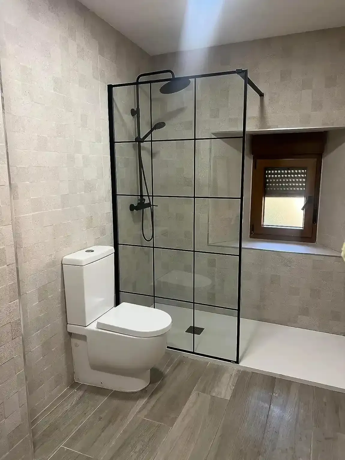 Un baño moderno con un inodoro blanco junto a una ducha a ras de suelo con marco negro y grifería negra mate.