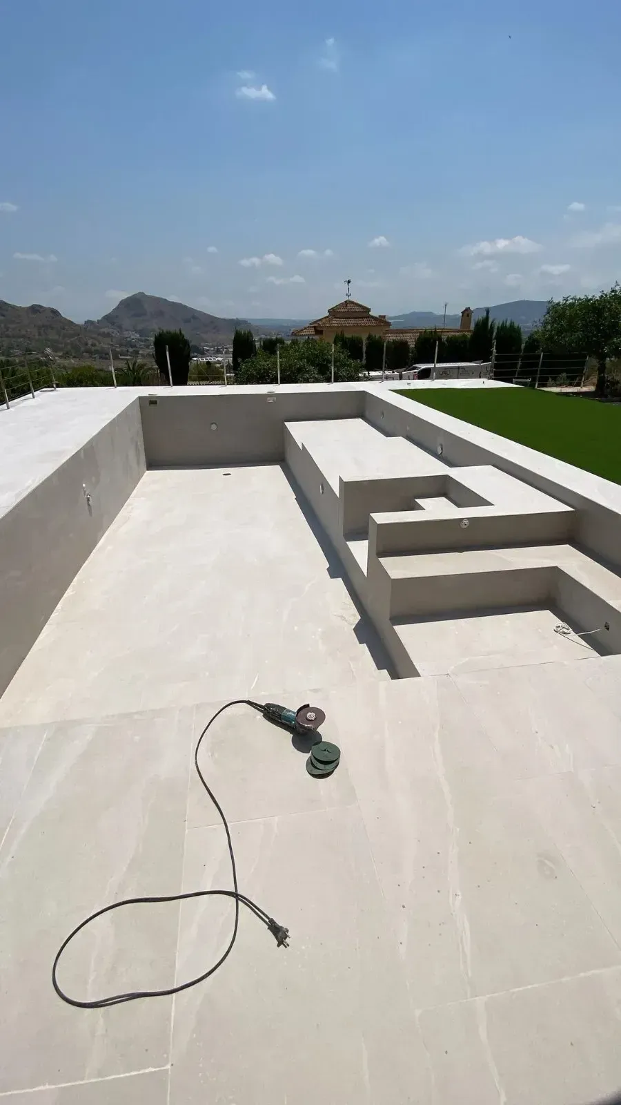 Una piscina o terraza vacía de piedra de color claro en construcción, con una herramienta eléctrica en el suelo.