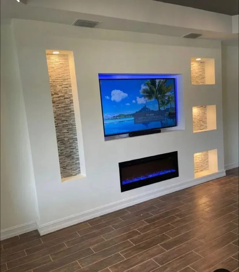 Una pared decorativa con chimenea integrada, televisor empotrado y nichos laterales acentuados.