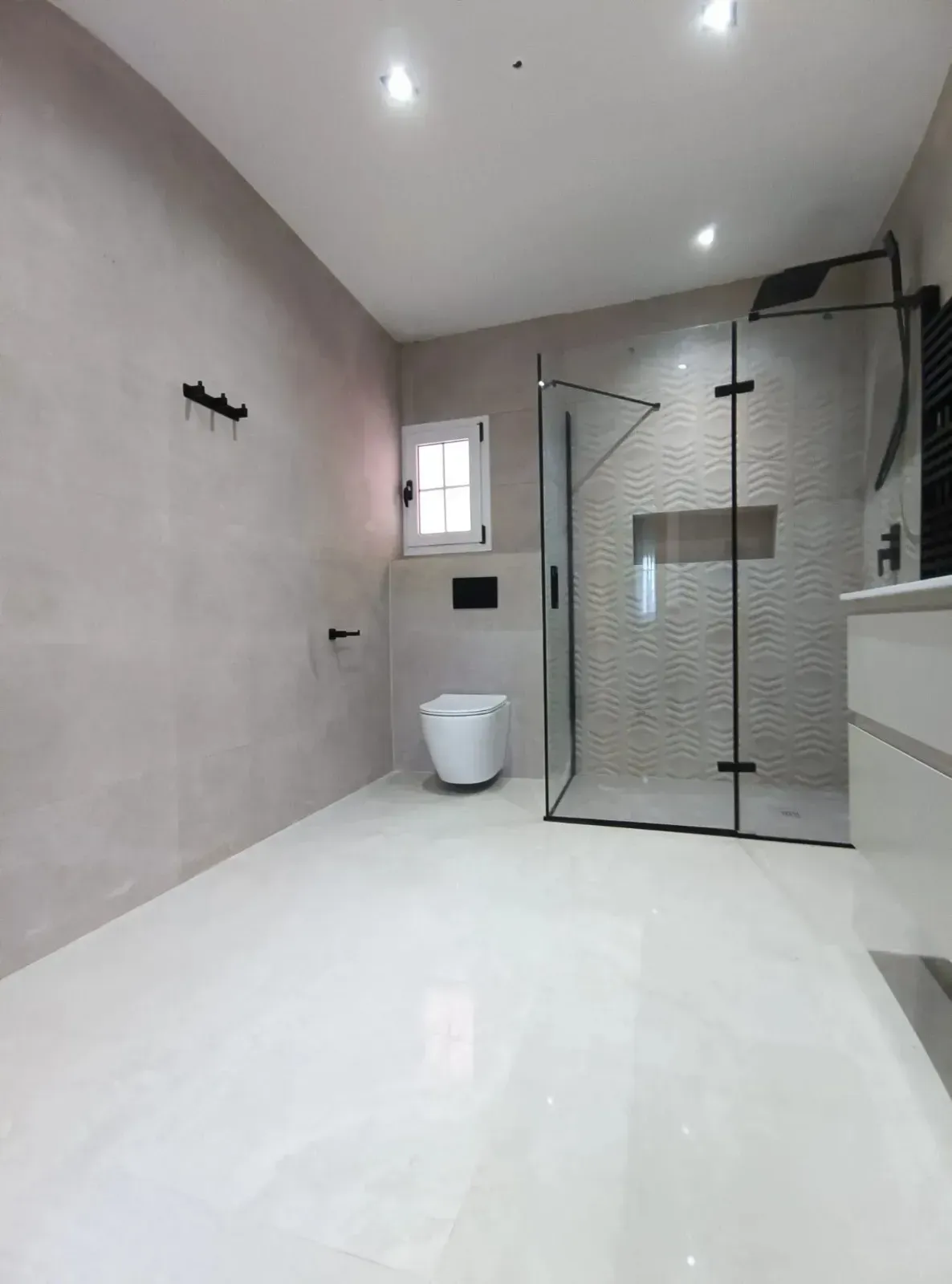 Un baño moderno y minimalista con suelos blancos brillantes, paredes beige, inodoro suspendido.