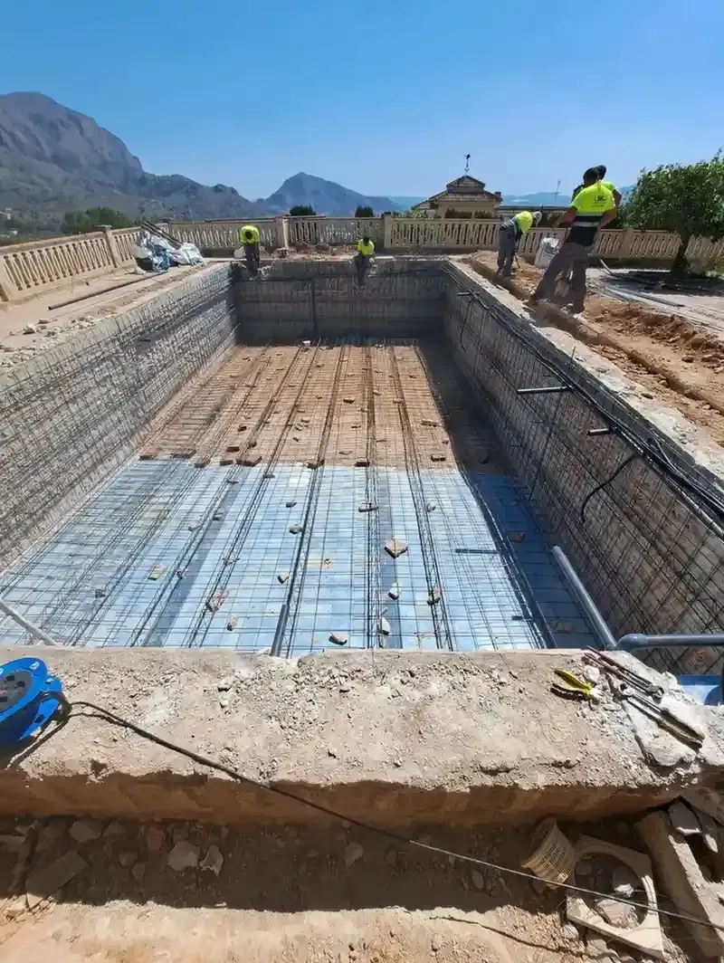 Obreros de la construcción, con chalecos reflectantes, trabajan en la estructura de barras de refuerzo metálicas.