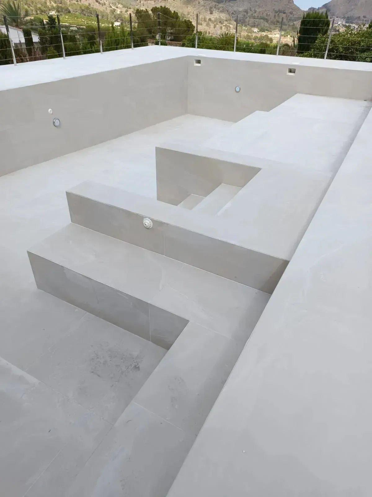 Una piscina vacía de hormigón de color claro, con escalones escalonados y asientos incorporados.