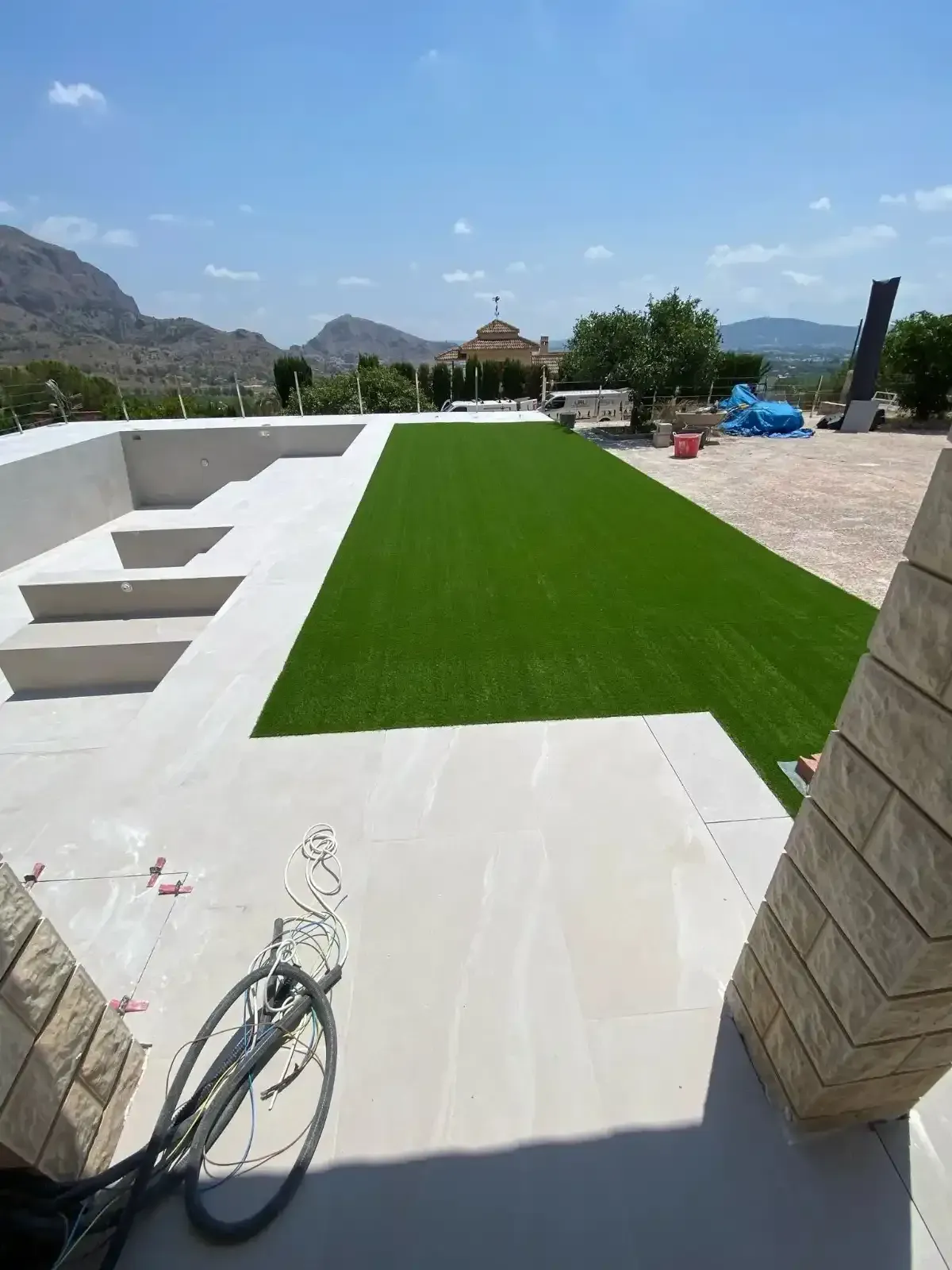 Un patio blanco con escalones conduce a una zona rectangular de césped artificial verde al aire libre.