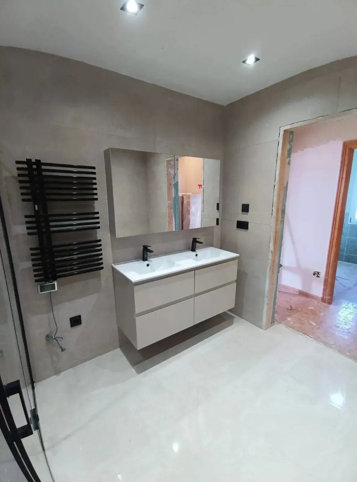 Baño moderno con lavabo doble con grifería negra mate, radiador toallero negro y azulejos.