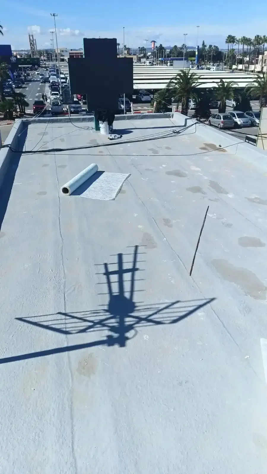 Un tejado plano de color gris bajo un cielo azul despejado, con una gran cruz oscura y la sombra de una antena .