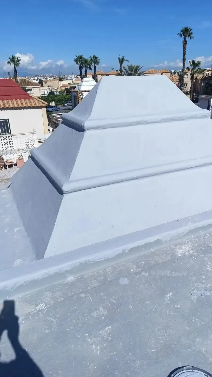 Una rejilla de ventilación de color gris claro con forma de pirámide sobre un tejado plano y pintado,.