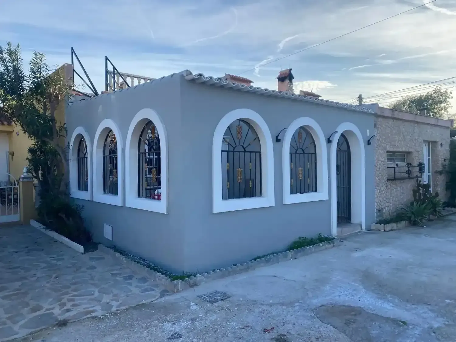 Vista de esquina de una casa azul claro con múltiples ventanas arqueadas con marcos blancos .