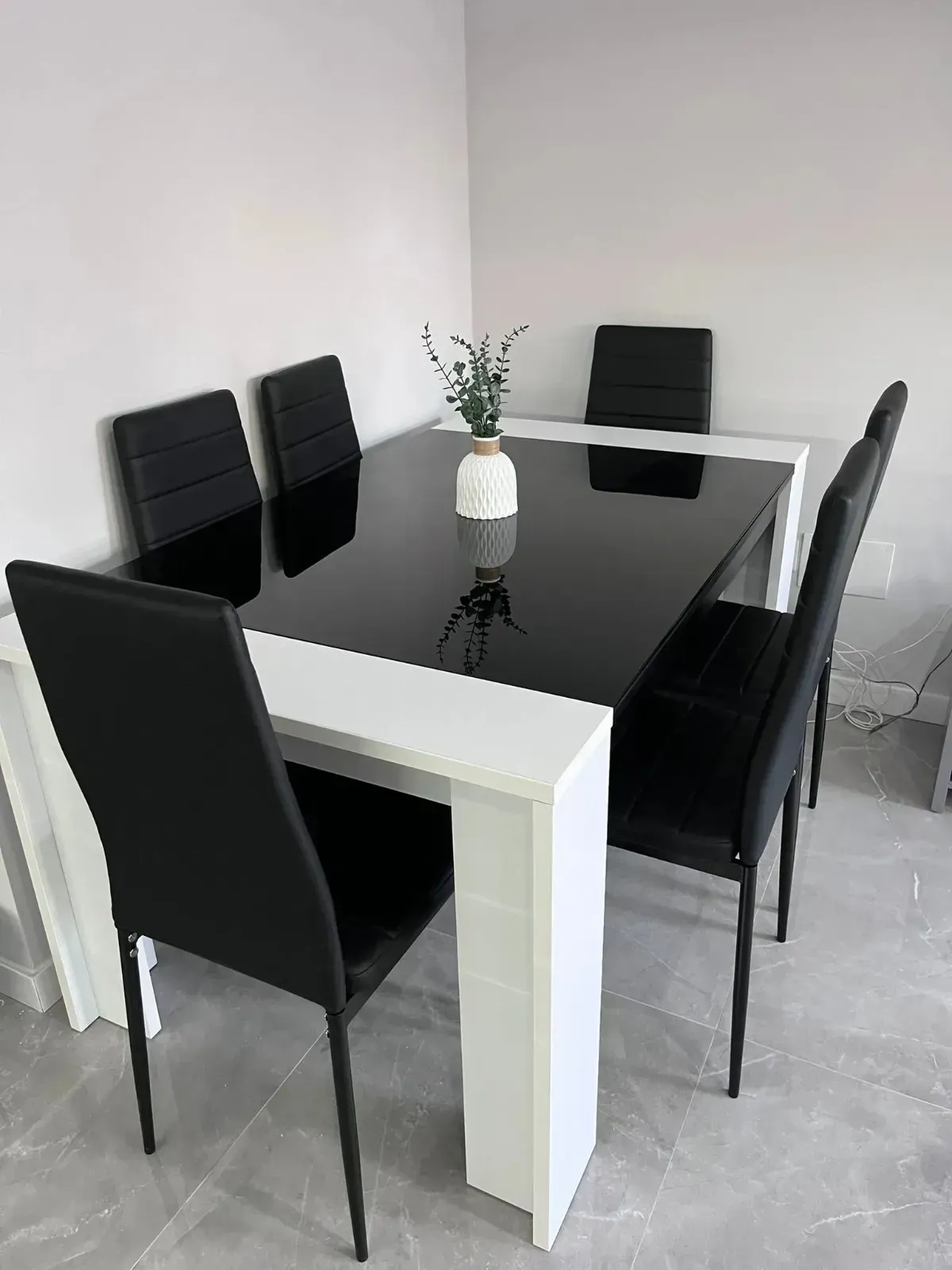 Una mesa de comedor blanca con tablero negro brillante y cuatro sillas negras, colocadas en una habitación.