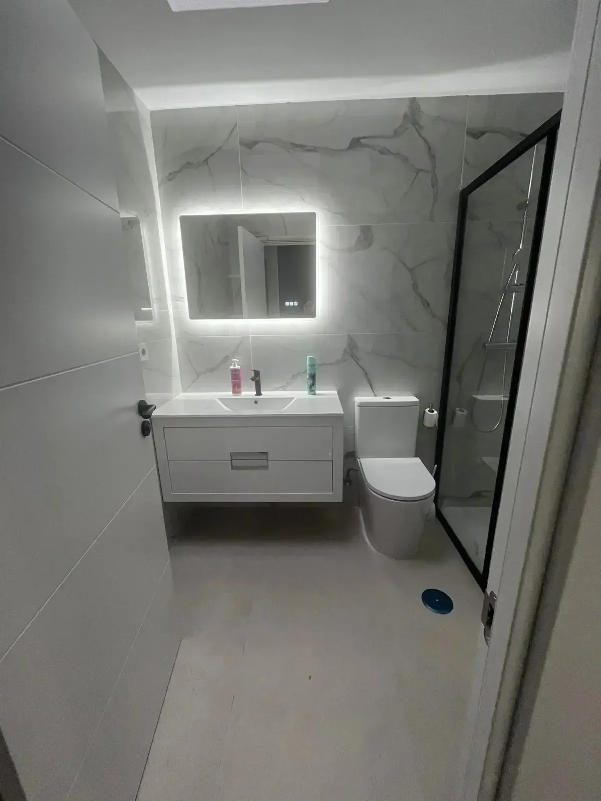 Baño moderno con paredes con diseño de mármol, un tocador blanco con espejo iluminado, un inodoro .