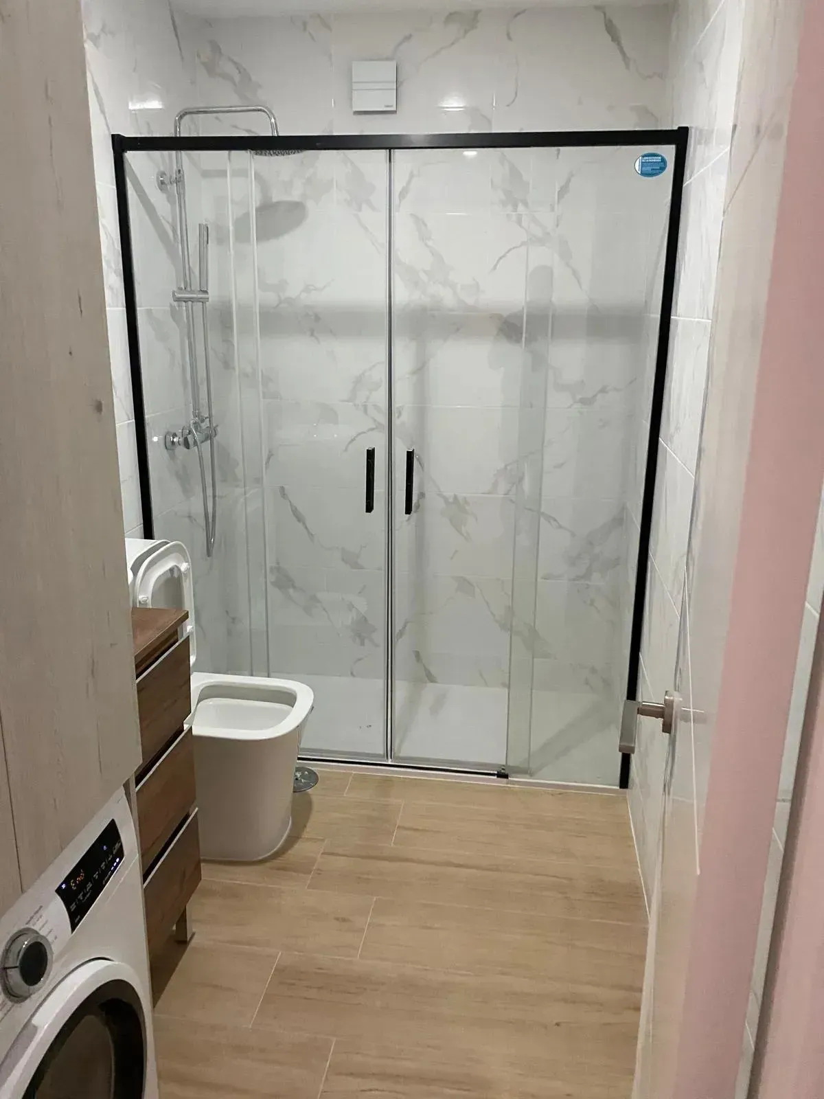 Un baño con ducha a ras de suelo con puertas de cristal con marco negro, paredes revestidas de azulejos.